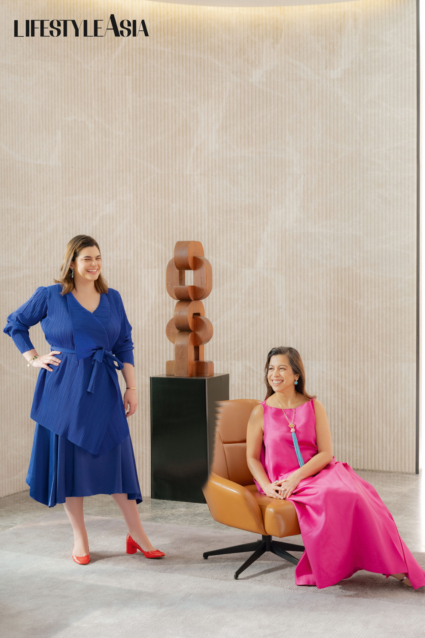 On Mariana (left): Royal blue pleated wrap top and skirt, ADOLFO DOMINGUEZ. On Ginbee (right): Fuschia silk gazar dress, ADOLFO DOMINGUEZ; Earrings, JJ JIAO JEWELRY; Necklace from JUL B DIZON.