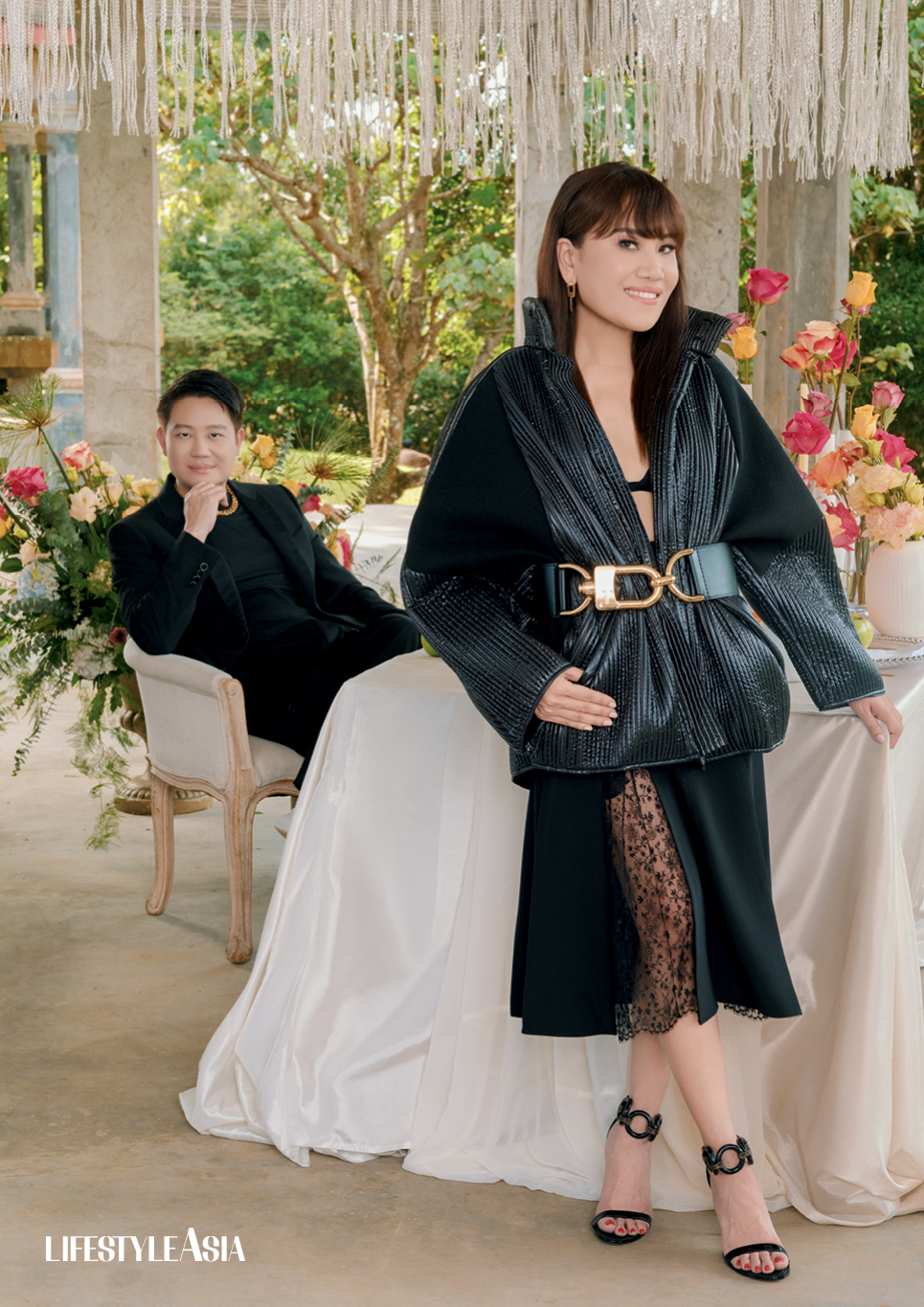 On Z: Black monogram printed blazer, pants and chunky gold chain, LOUIS VUITTON; On Aivee: Black quilted lurex jacket, lace skirt and belt LOUIS VUITTON.