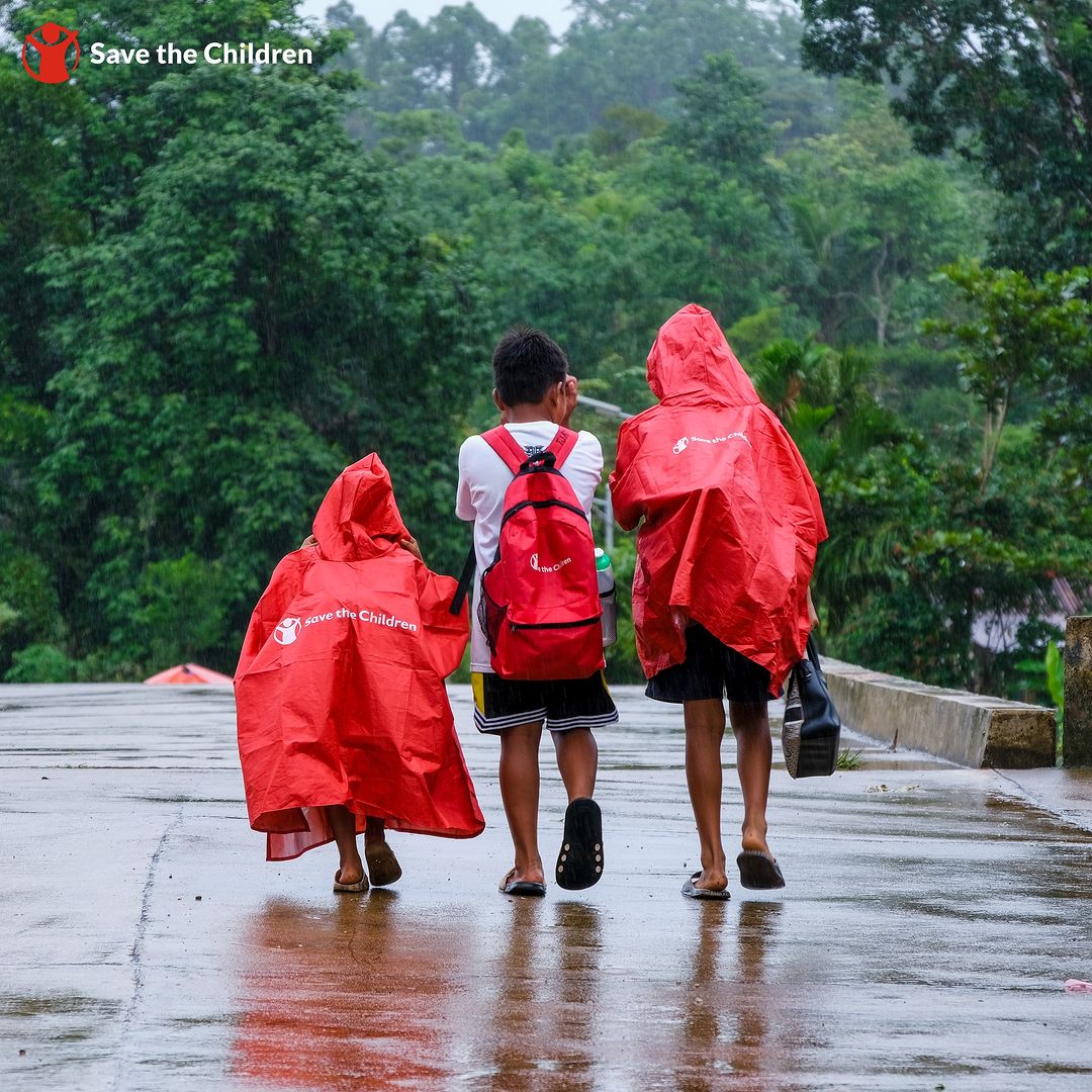 Children with Save the Children raincoats and bags to keep them weather-ready