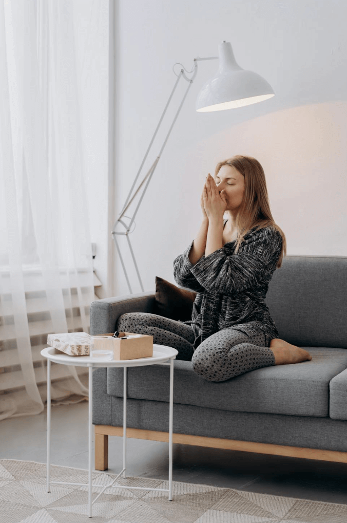 Woman praying, sitting on gray couch