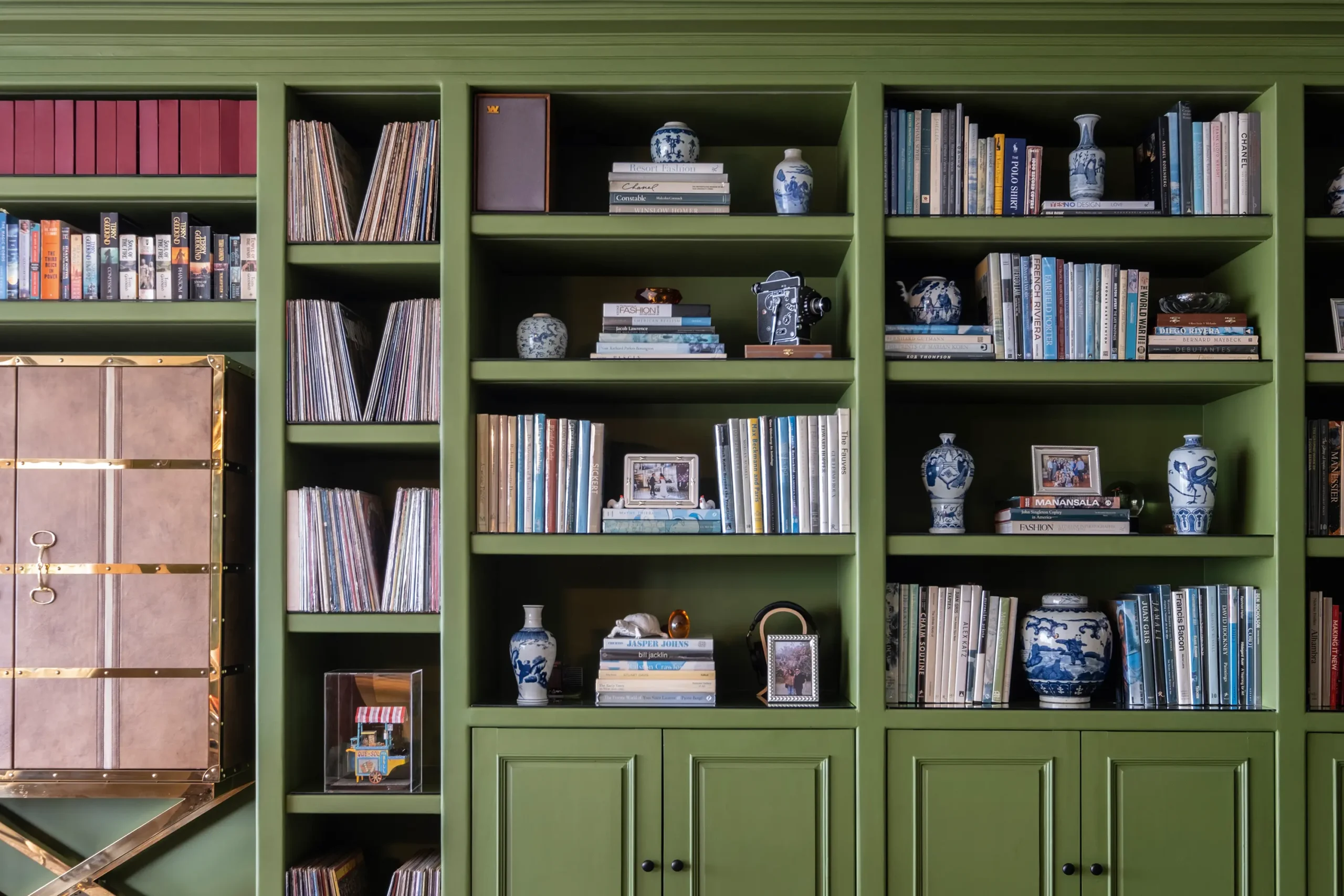 Green shelves with antique porcelains, new and vintage coffee table books, and heirloom pieces passed down from their families. The bottom shelf features a miniature by Chino Yuseco