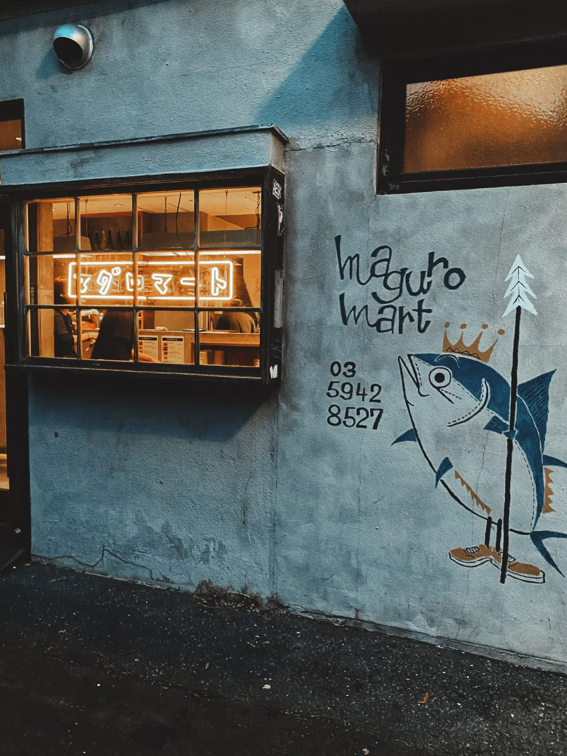 The exterior of Maguro Mart in Tokyo is adorned with vibrant yellow neon signage, whimsical illustrations, and a sleek, modern aesthetic