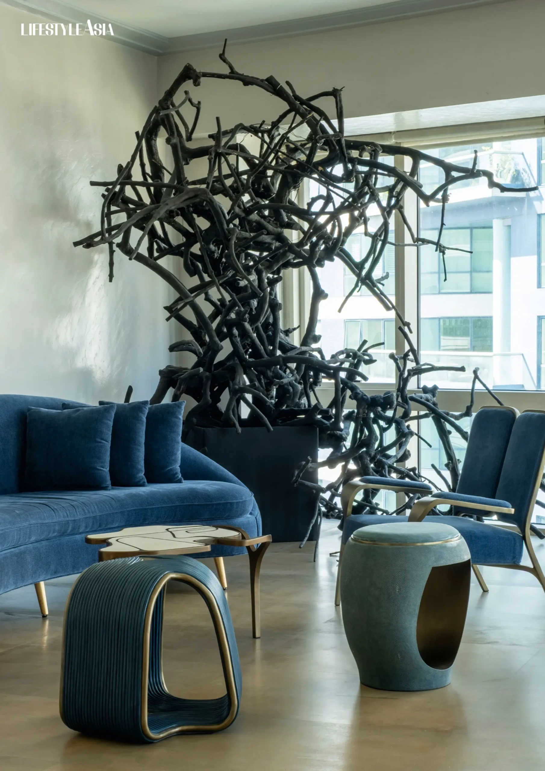 The black installation of twisted, interwoven branches—originally designed for a dinner party—now anchors the space behind the deep blue sofa, serving as an organic yet architectural focal point in the living room