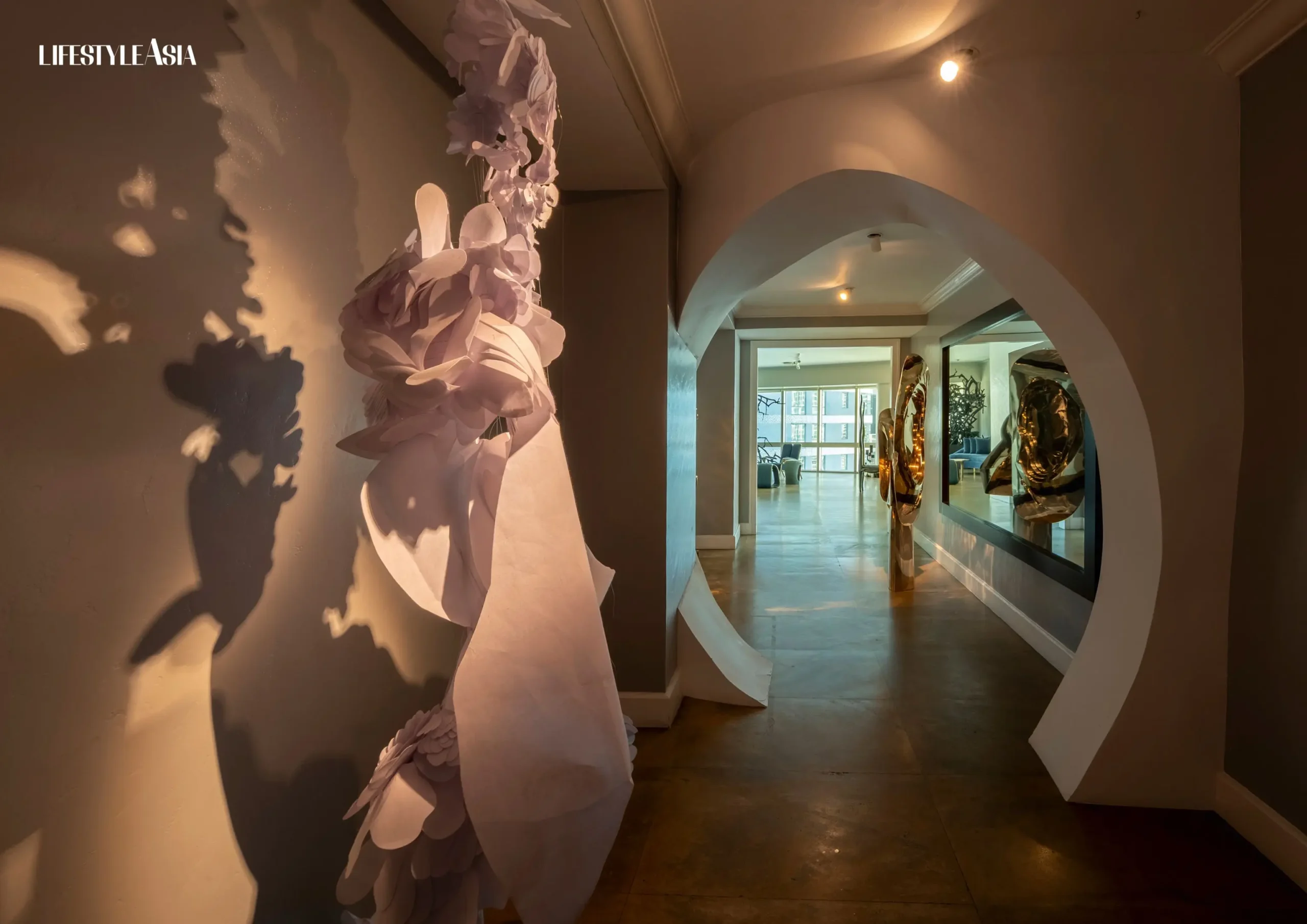 The entryway features Bea Valdes’s feather-like white sculpture, with an oval archway framing the living space beyond acting as a sensory threshold