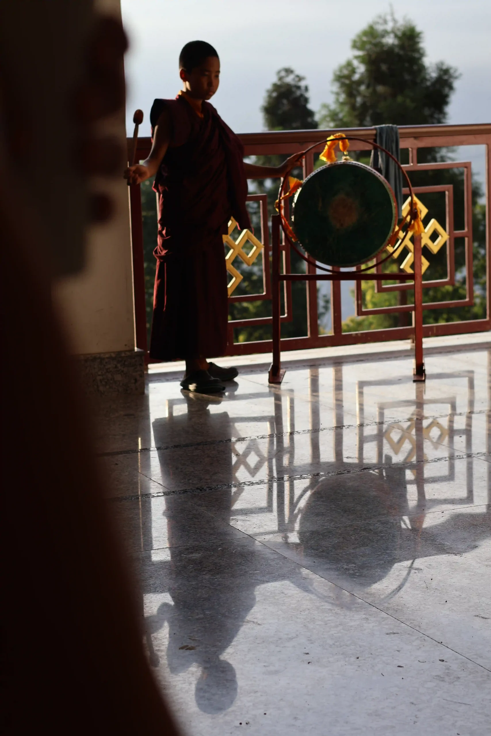 A young monastic student drums to signal the start of morning prayer at Nedo Monastery, Sikkim, India