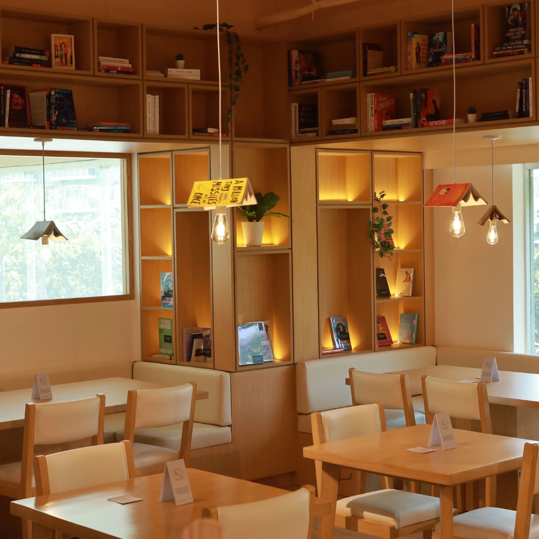 Cozy bookstore cafe with wooden shelves, warm pendant lights, and tables set for seating.