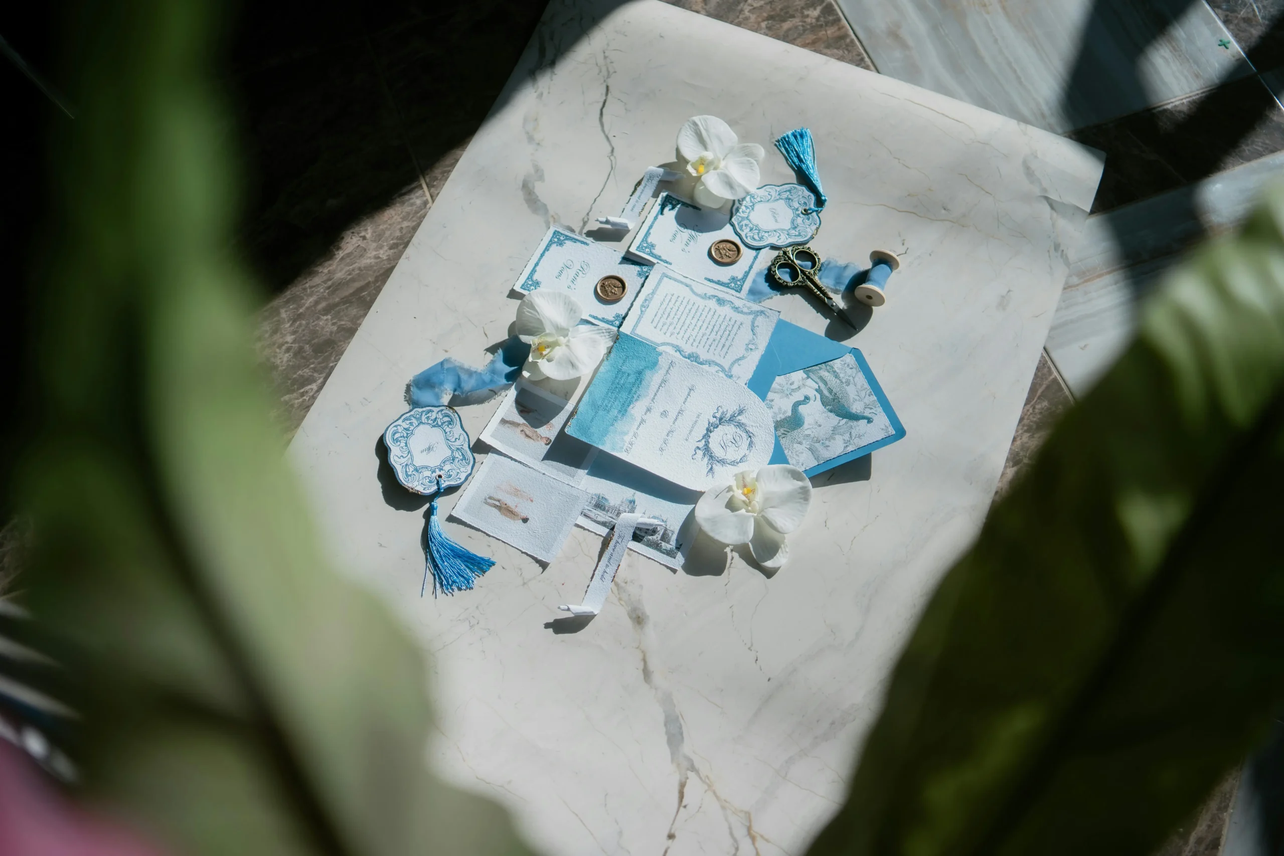 Flat lay of blue and white wedding invitations, flowers, and stationery arranged on a marble tabletop.