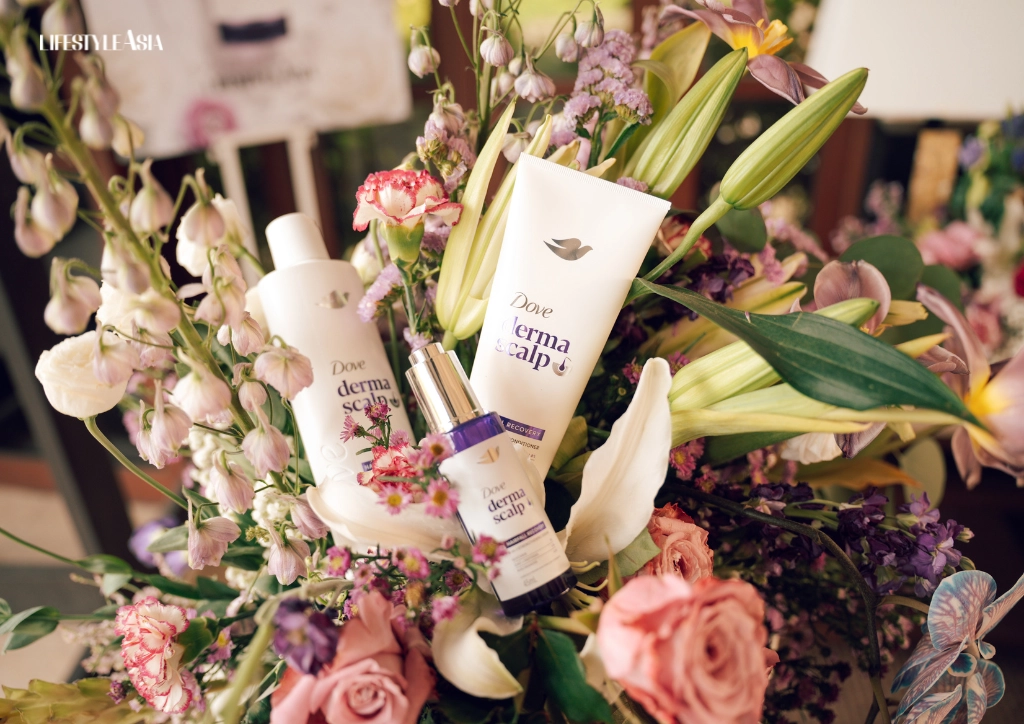 Flower arrangement with Dove DermaScalp bottles nestled among pink, white, and purple blooms; Lifestyle Asia logo in the top-left.