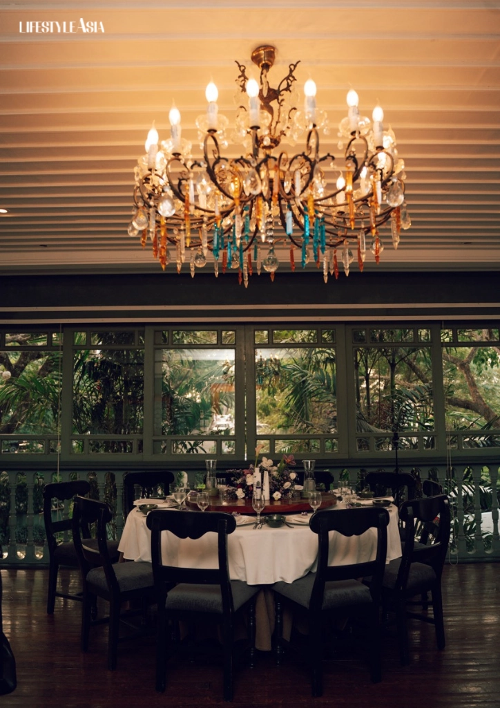Elegant chandelier hanging above a round dinner table set with white linens and a floral centerpiece.