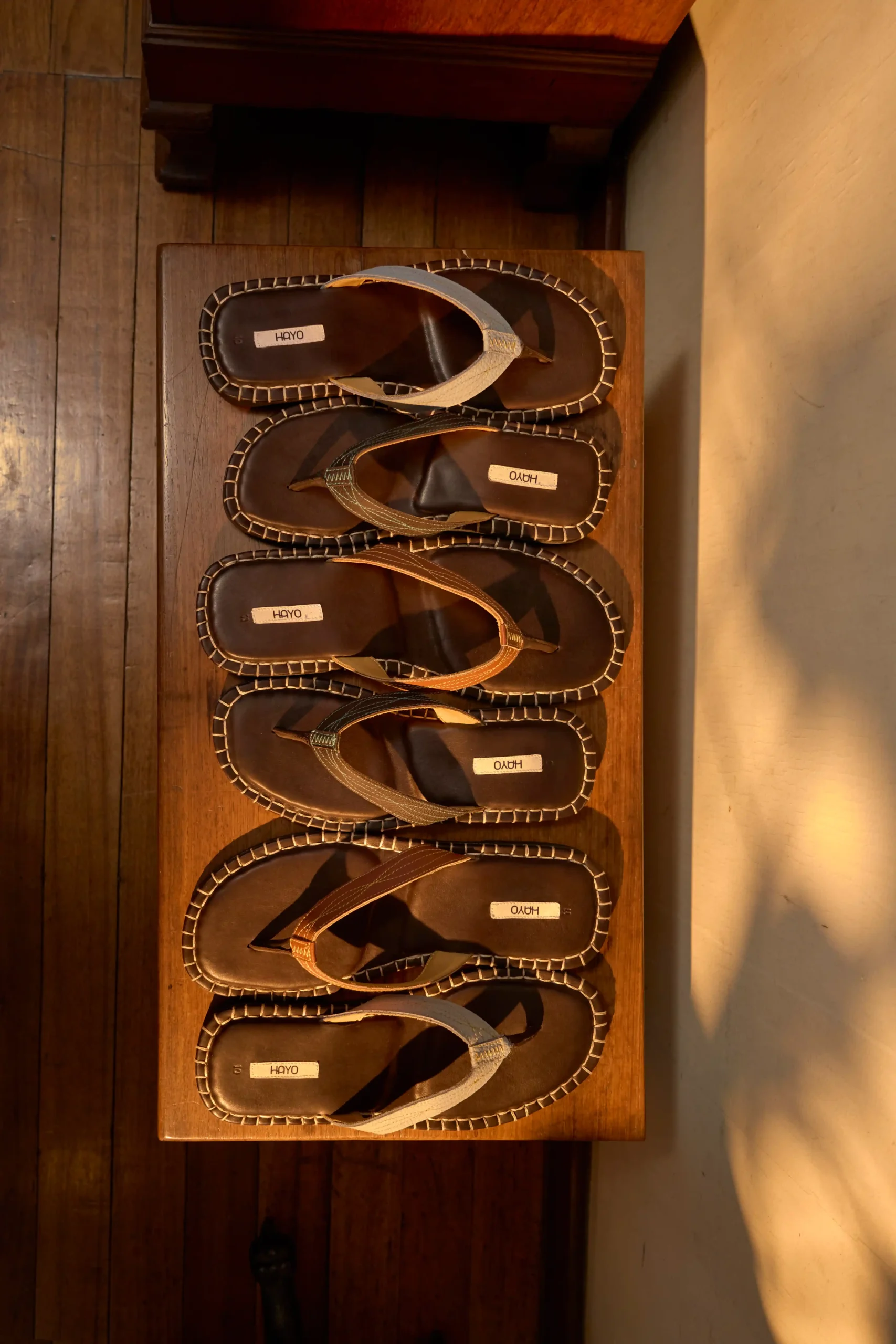 The Siesta Slippers by Hayo Footwear. Row of brown sandals with white stitching displayed on a wooden shelf, brand labels reading HAYO visible