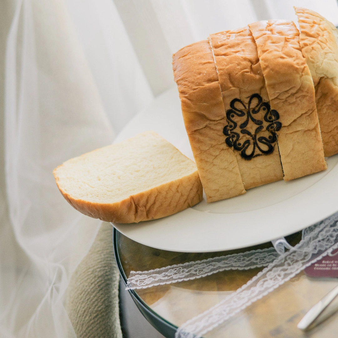 Loaf of white bread with a decorative black stamp on the crust, partially sliced and placed on a white plate.