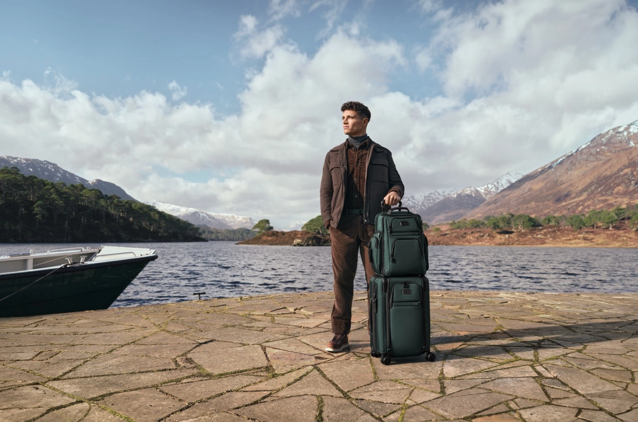 Lando Norris pictured with the Alpha TUMI Brief Pack and Alpha Dual Access Expandable 4 Wheeled Carry-On in Deep Pine