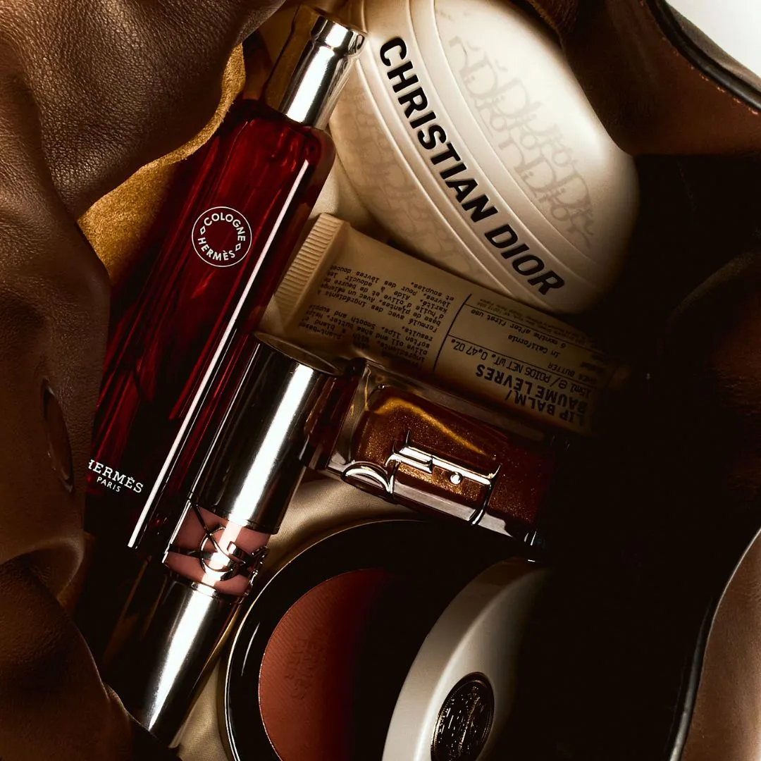 travel kit Travel-Sized Beauty Items To Take On Your Next Trip Mini Flamenco Clutch In Nappa Calfskin by LOEWE; Nomade Cologne by HERMÈS; Le Baume by DIOR; Lip Balm by LE LABO; Loveshine Lipstick by YSL; Dior Lip Oil by DIOR; Rose Hermès in Rose Abricot by HERMÈS.